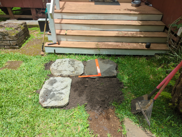 photo looking toward the front steps; three paving stones are set in a bed of dark sand; a framing square and various yard implements are visible and there's a Thermacell mosquito repellent on the steps