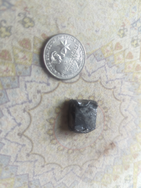 photo of a beaten-up wheel balancing weight next to a US quarter dollar coin for scale