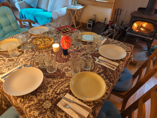 photo of the brunch table with six place settings, an anterium, a quiche, stuffed dates, and in the background a fire roaring in the woodstove