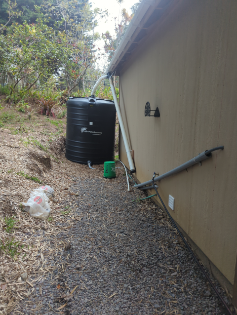 photo showing a water tank fed by rain gutters with a first-flush diverter and a nearby spigot on the wall