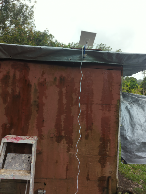 photo of the chicken door solar panel mounted on the coop roof, with the power cable dangling toward the (not visible) door