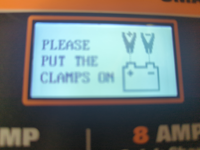 photo of the display of a lead acid battery charger saying PLEASE PUT THE CLAMPS ON