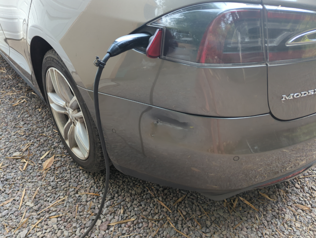 photo of an electric car's left rear quarter panel showing a large dent in the bumper