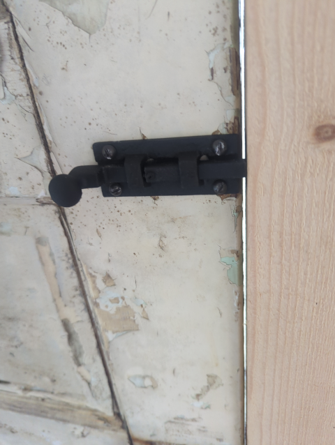 photo of a black iron door bolt on a well-weathered door
