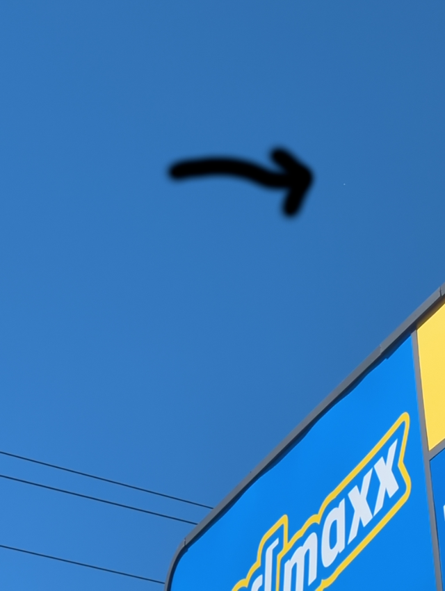 balloon is a tiny, barely visible dot in the sky above a shopping center sign