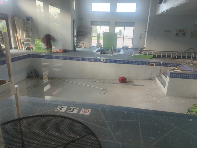 photo of a pool obviously in no state for swimming, with construction equipment and supplies in and around it and no water
