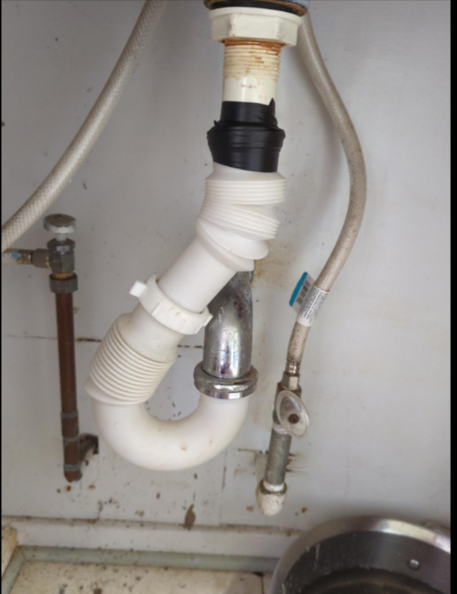 a photo of the underside of a bathroom sink with a wildly-contorted arrangement of flexible pipes