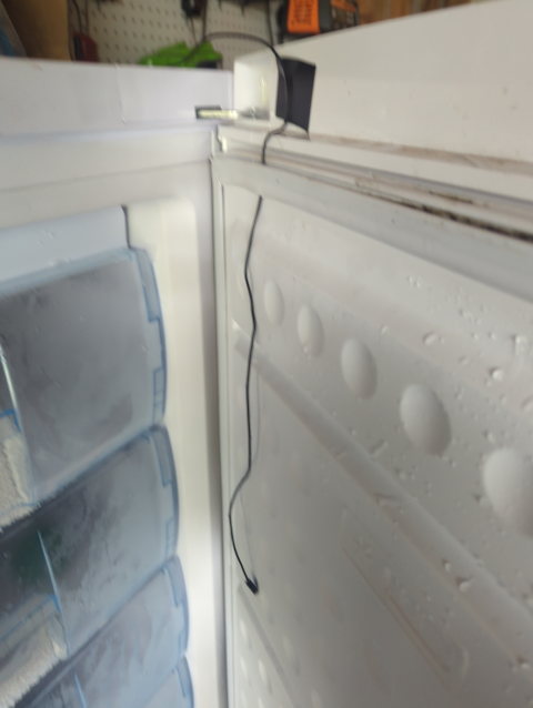 photo showing an open upright freezer door with a small wire threaded through the insulating gasket and hanging down into the freezer space