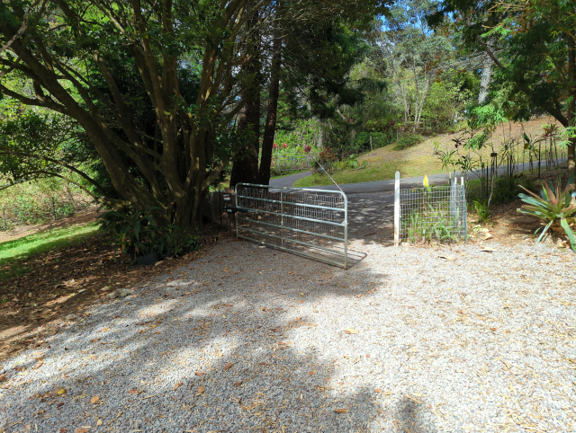 photo of a pipe gate across a gravel drive with an electric closer installed, in mid-swing