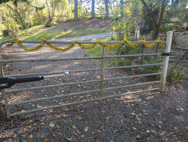 photo of a field gate with a gold garland draped on the top; a plastic Frosty the Snowman is in the background