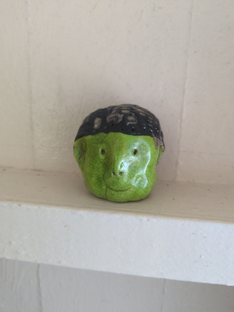 photo of a small ceramic head with a green smiling face and black hair with metallic highlights