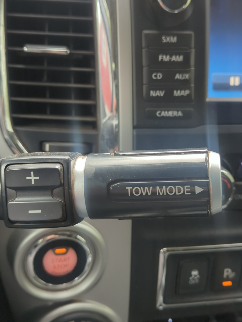 photo of a part of the Nissan dashboard with a steering column stem completely hiding the defogger buttons behind a label reading "TOW MODE>"