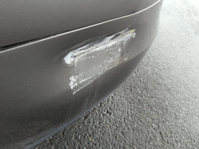 close-up photograph of a car bumper with a large dent and scrapes