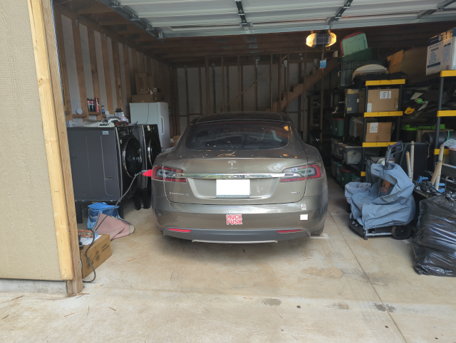 photo of Joulee the Free Salvage Tesla in the garage, with the washer and dryer to the left and accumulated junk treasures to the right