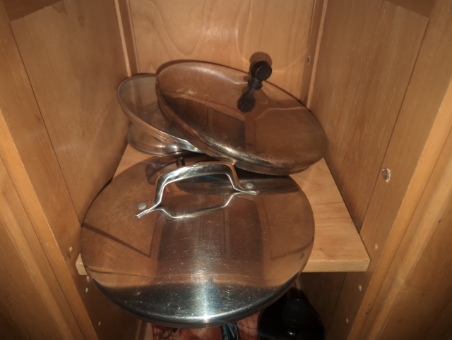 photo of a low shelf in a kitchen island with a haphazard heap of pot and pan lids