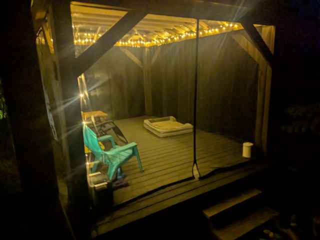 photo from the outside of the pavilion at night, with a string of LED holiday lights illuminating the inside along the ceiling