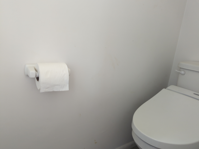 photo of the half bath in the studio, showing the tissue roll dispenser (with tissue) mounted on the wall and the toilet with bidet seat to the right