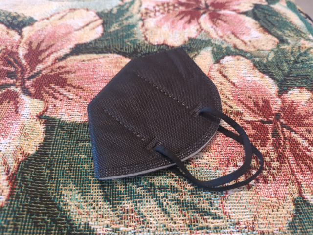 photo of a black KN95 respirator mask resting on floral-pattern damask cloth
