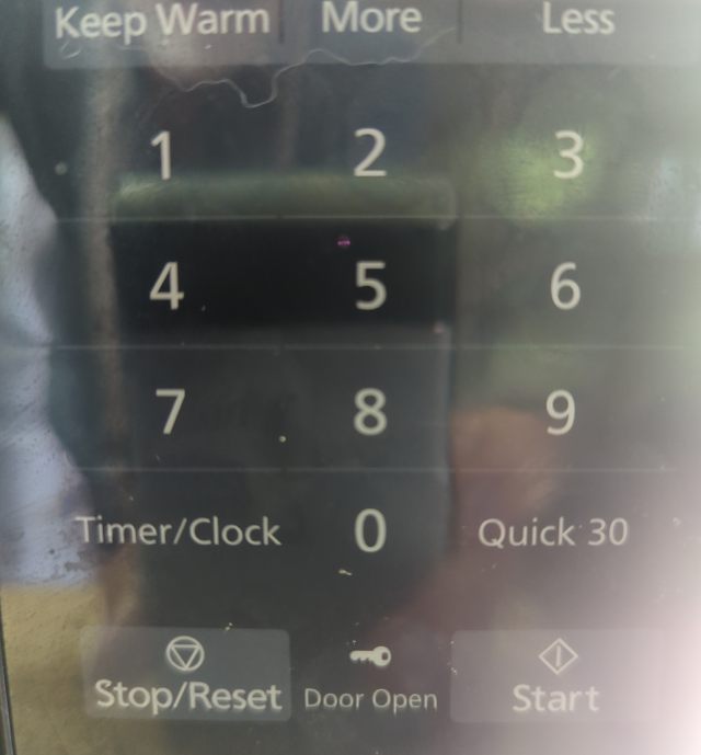 photo of the membrane keypad of my microwave oven replete with reflected images from the kitchen