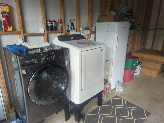 photo of a new, white Samsung dryer installed to the right of an older, fancier LG front-load washer; a white upright freezer is to the right of the dryer