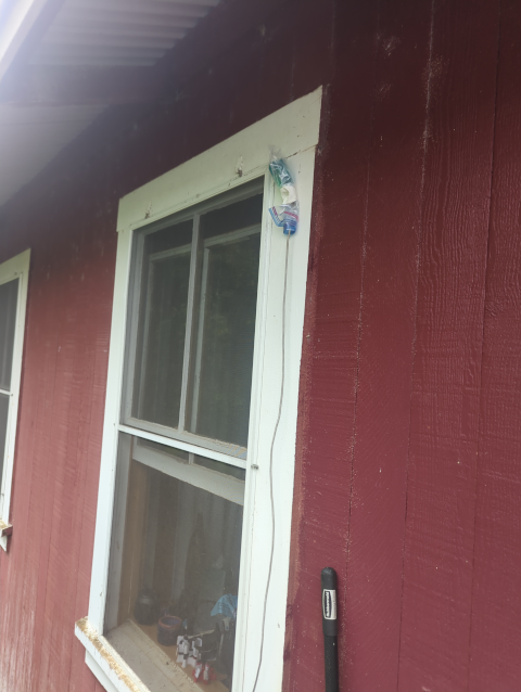 photo of the window behind my desk, from the outside, showing the Meshtastic node attached to the wall with a cable running through the window