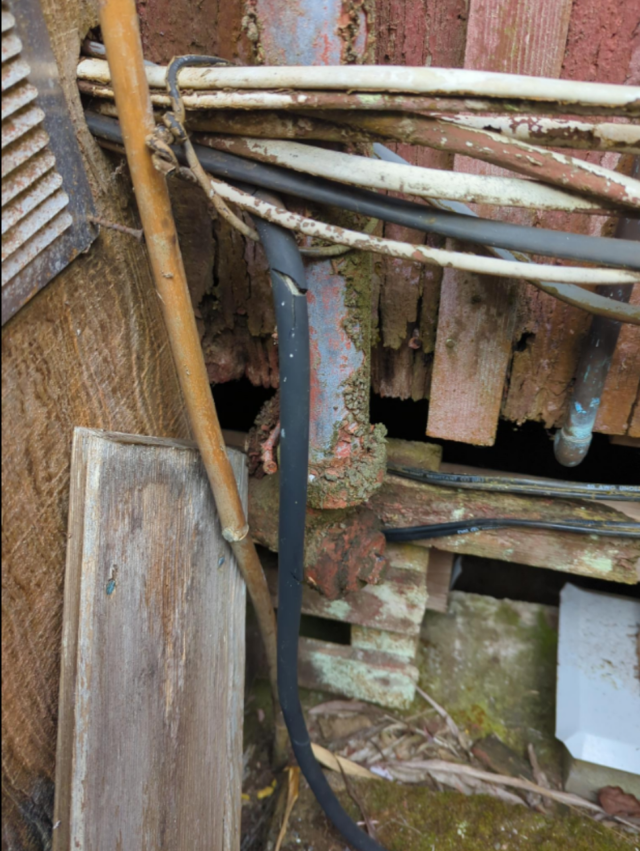 a photo of an old, paint-covered, rusted, dirty drain cleanout surrounded by Romex wires