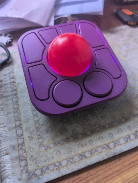 photo of an assembled, purple Ploopy A+ trackball with six buttons, two scroll wheels (each also a button) and a lighted red trackball