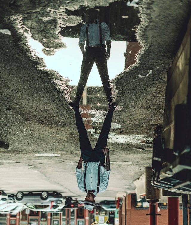photo of a man straddling a puddle; the photo is upside down, but the man's reflection in the puddle appears right side up