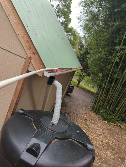 photo looking down on the gutter and water tank with a long white pipe with a red scoop on the end, being pushed along the gutter