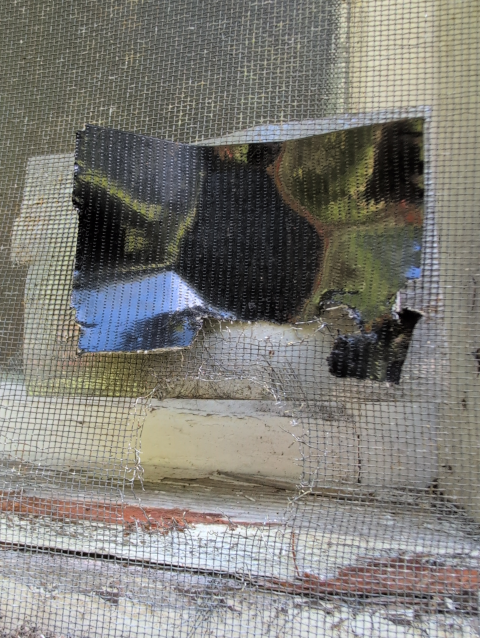 photo of a window screen showing one hole patched with Gorrilla Tape and another hole right below it
