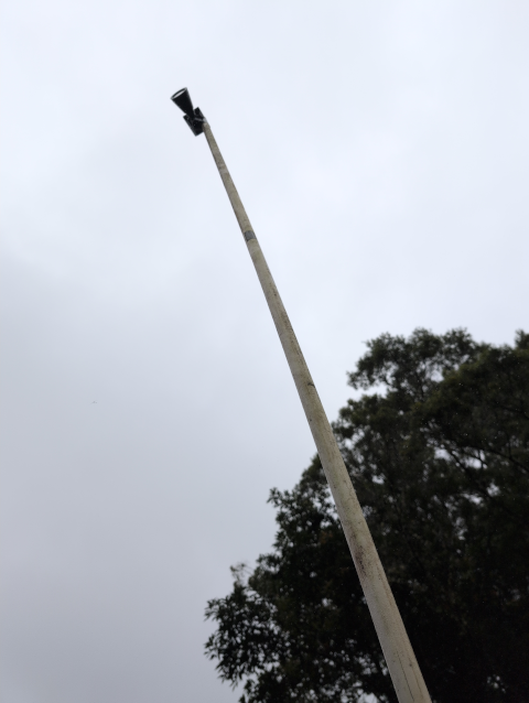 photo looking up at a tall, vertical length of dirty white PVC pipe with what appears to be a simple solar garden spotlight taped to the top of it -- but we know it's an autonomous solar-powered mesh node!
