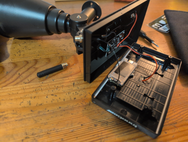 photo showing the solar spotlight case opened with the T114 stuck in a glob of mounting putty and the antenna connector bolted into the new hole in the case