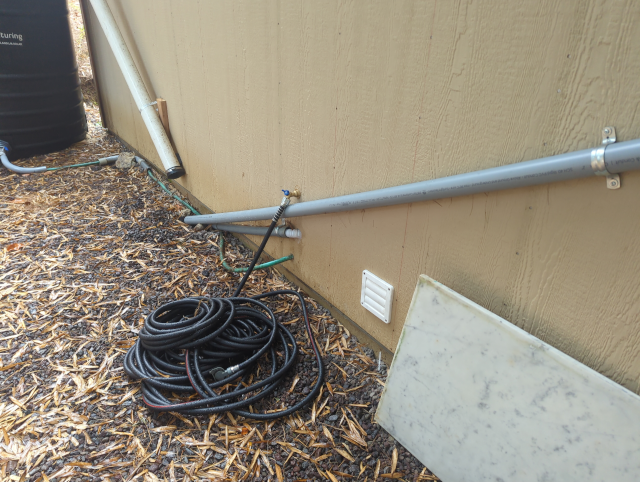photo of the side of the garage showing a newly-installed water spigot with a long hose attached