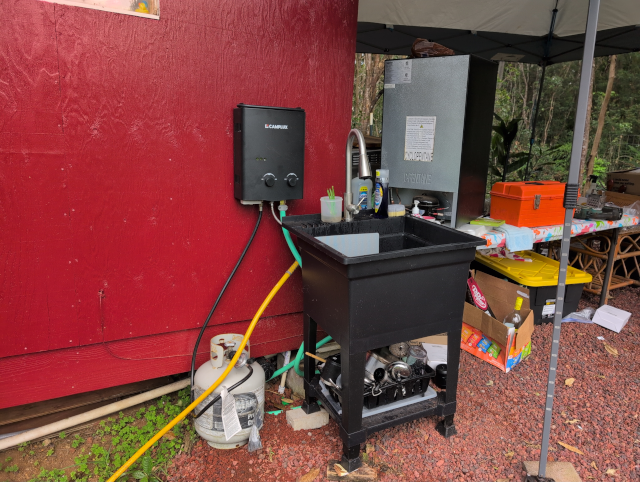 photo showing a camping propane hot water heater mounted on the wall of the studio next to the kitchenette sink