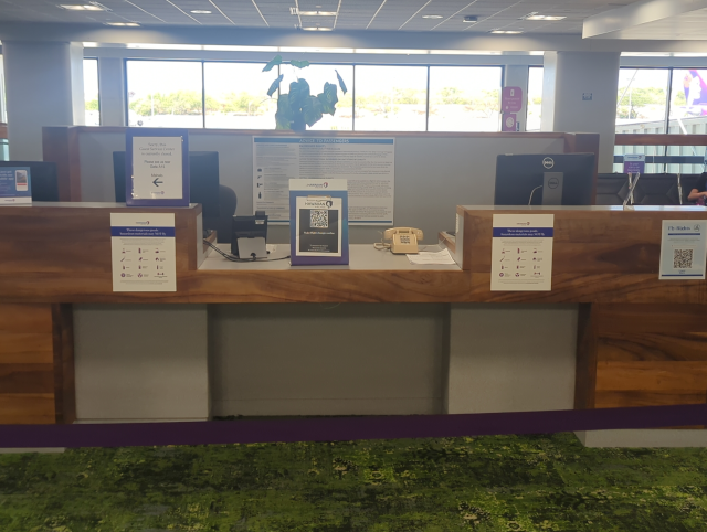 photo of a desk in a busy airport, with no people at the desk but a conventional wireline telephone facing the customer side