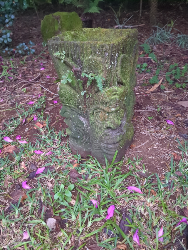 photo of a moss-covered concrete planter with tiki faces on it