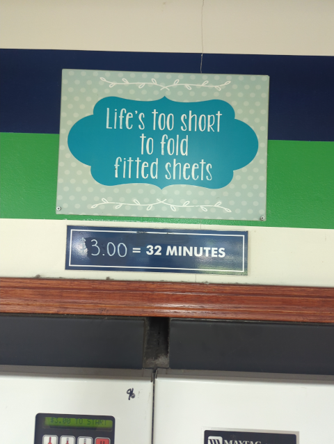 photo of a sign on the wall of a laundromat that reads "life is too short to fold fitted sheets"