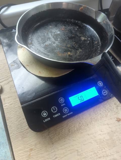 photo of an iron skillet on an induction burner; between the skillet and the burner is a flour tortilla