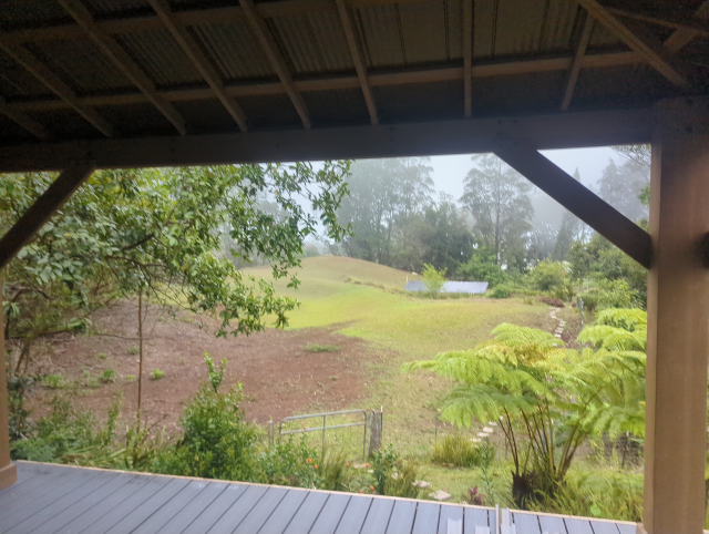 photo from inside the pavilion showing the misty pasture and solar panels framed by the pavilion posts and roof