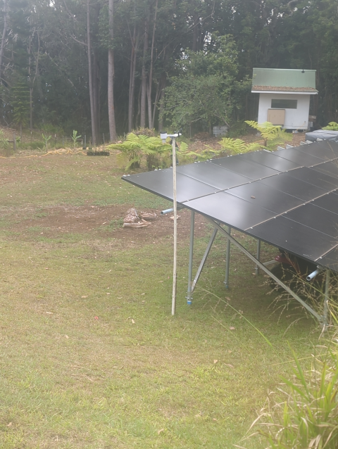 photo of an outdoor weather station mounted next to an array of solar panels