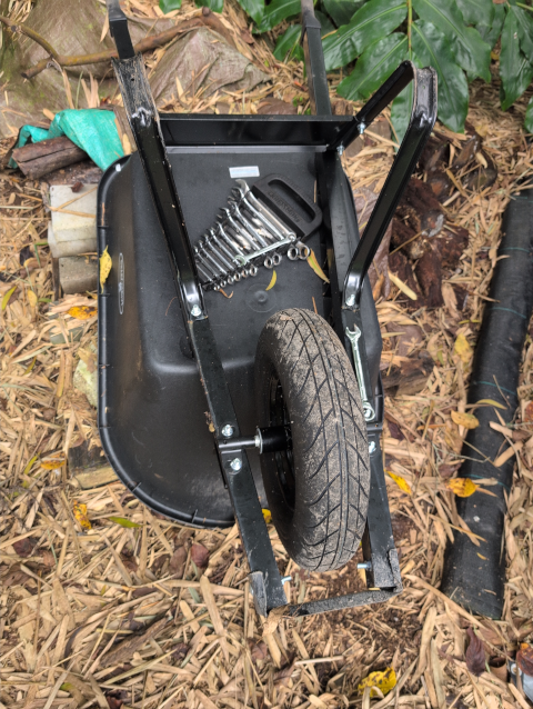photo of a black wheelbarrow upside down over brown bamboo leaves; a set of combination wrenches is resting on top
